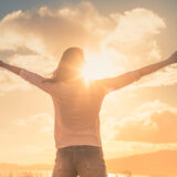 Young woman with hands up the morning sun light finding happiness, peace and hope in nature stock photo